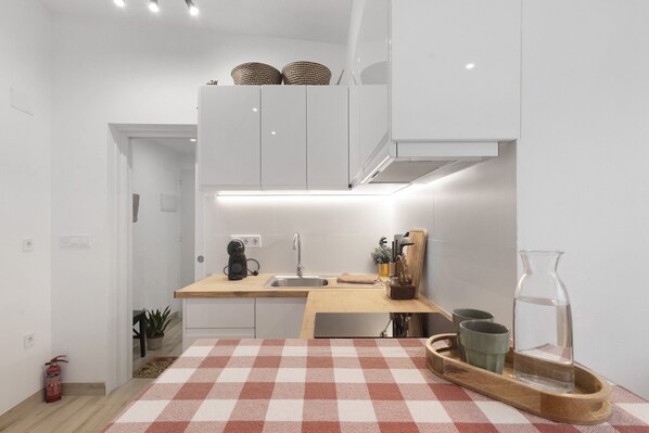 Une cuisine moderne avec des meubles blancs, un plan de travail en bois, un évier et un tapis de sol à carreaux.