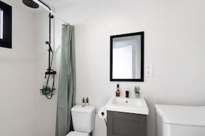 Et badeværelse med brusebad, toilet, vask og spejl.