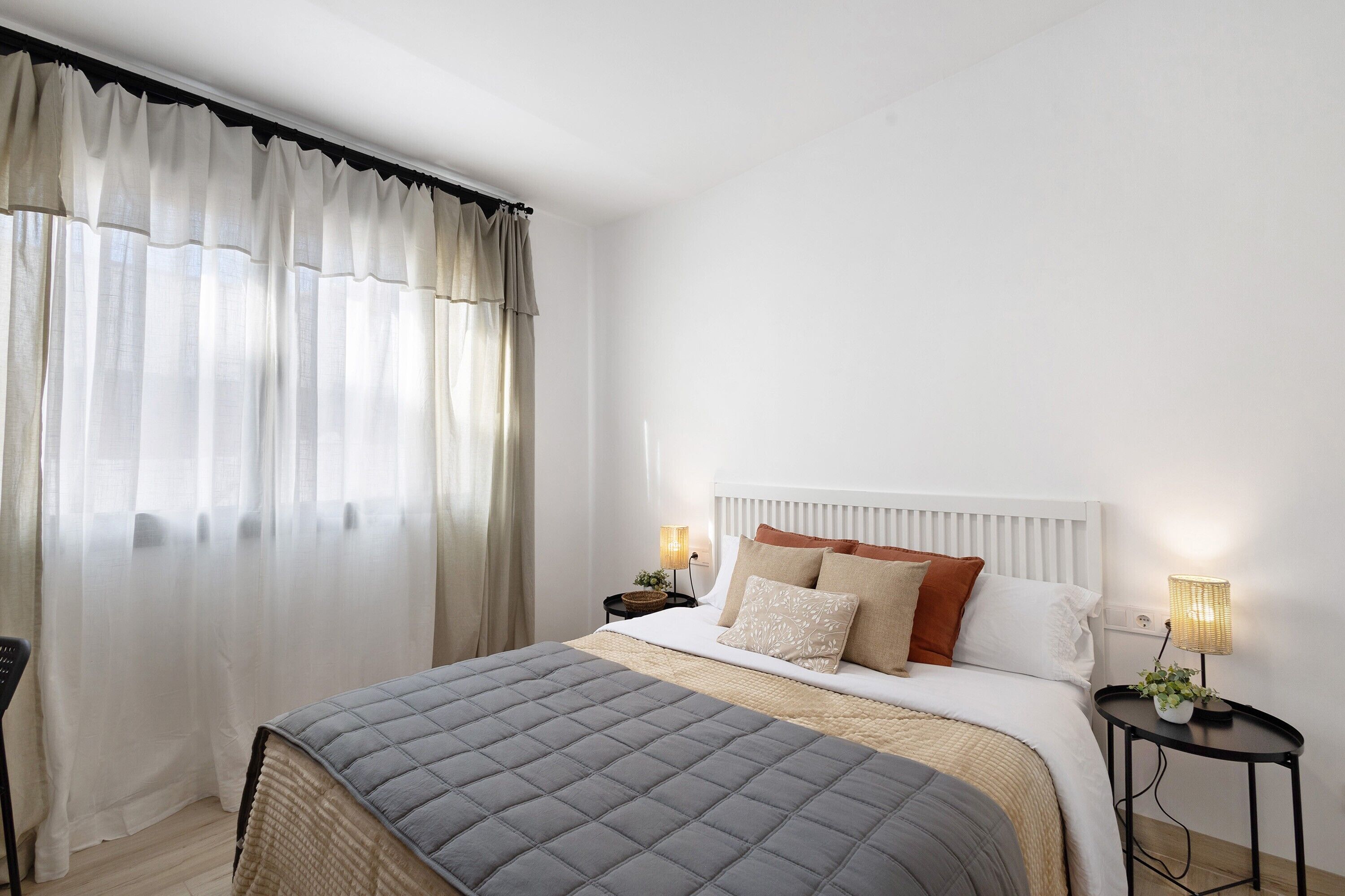 Un dormitorio ordenado con cama, mesitas de noche y ventana con cortinas.