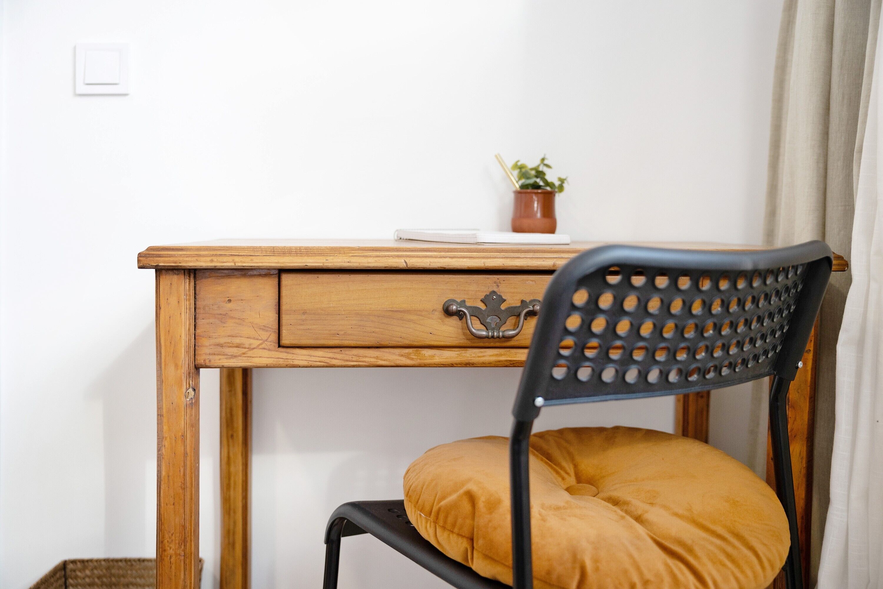 Un escritorio de madera con un cajón, una planta en maceta y una silla con cojín.