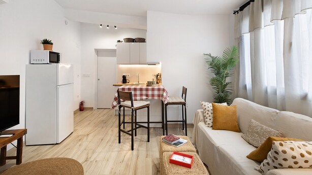 Un espacio habitable compacto con kitchenette, comedor y zona de estar con sofá y sillas.