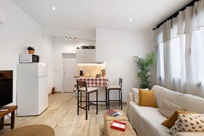 Un espacio habitable compacto con kitchenette, comedor y zona de estar con sofá y sillas.