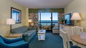 Ein Hotelzimmer mit einer Couch, einem kleinen Tisch, einem Fernseher und einem Balkon mit Meerblick.