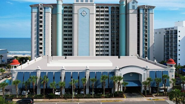 A large hotel with multiple floors, a prominent clock tower, and a view of the ocean. - Peace Awaits: Oceanfront King Suite 2nd Floor (Myrtle Beach)