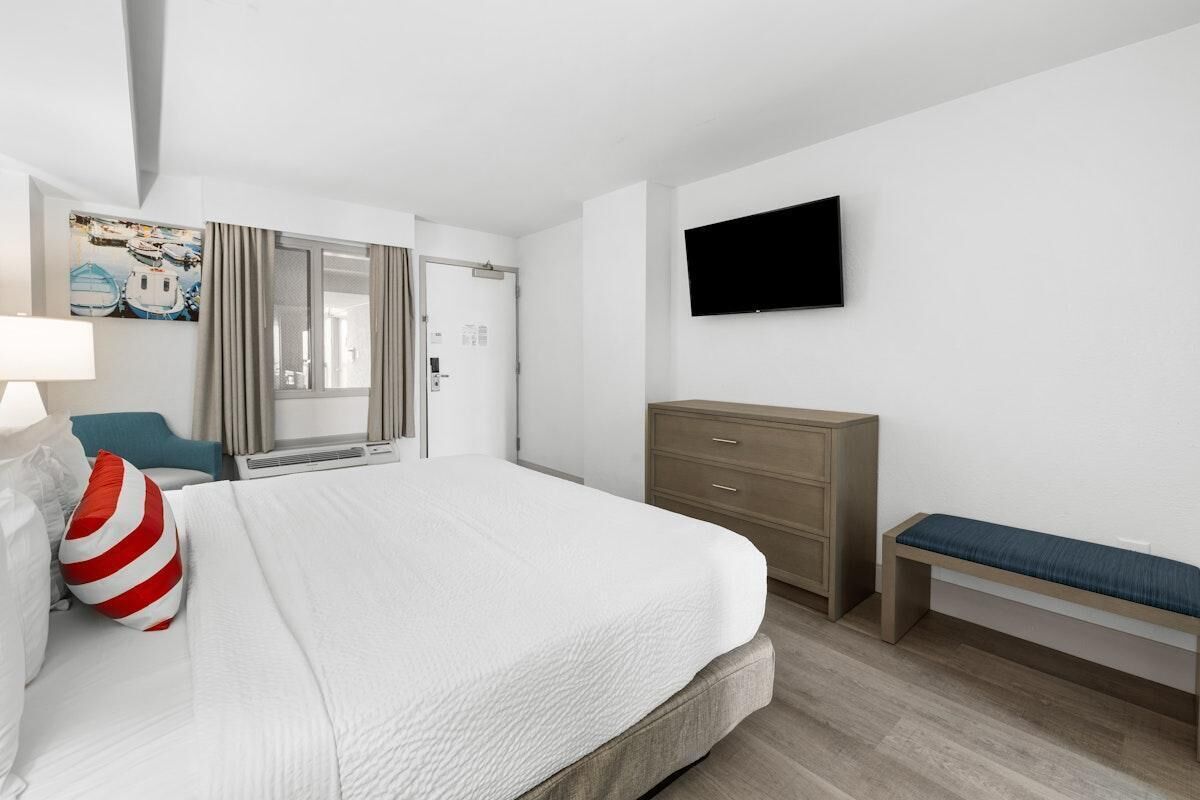 A hotel room with a bed, a bench, a TV, a wardrobe, and a window with curtains.