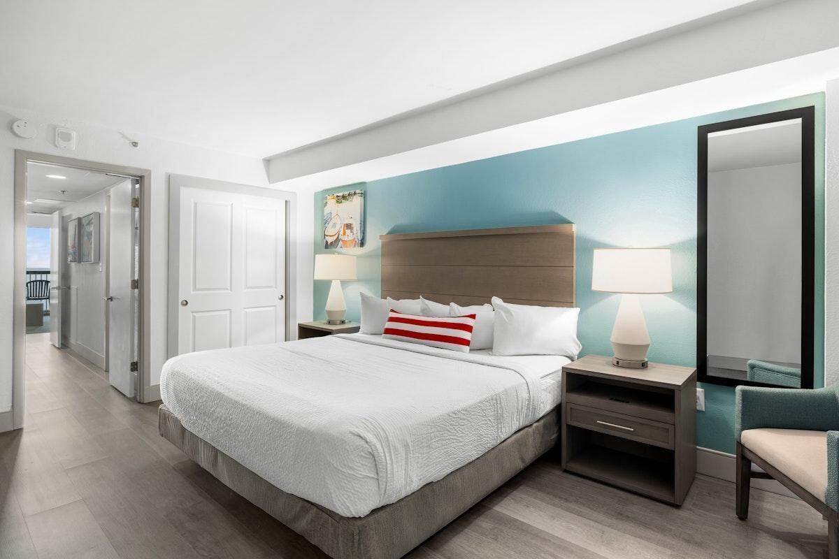 Ein modernes Hotelzimmer mit einem großen Bett, Nachttischen, einem Spiegel und Blick auf den Flur.