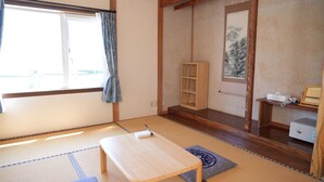 Um quarto japonês tradicional com tatames, uma mesa de madeira baixa, uma estante e um quadro na parede.