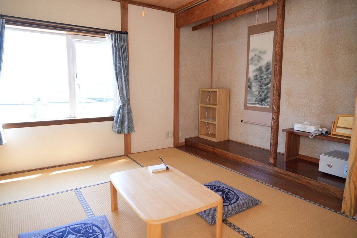 Una habitación tradicional japonesa con suelo de tatami, una mesa de madera baja, una estantería y un cuadro en la pared.