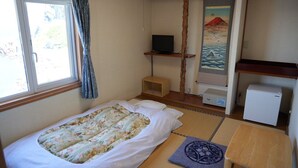 Quarto com cama, televisão, pequeno frigorífico e pintura de uma paisagem de montanha.