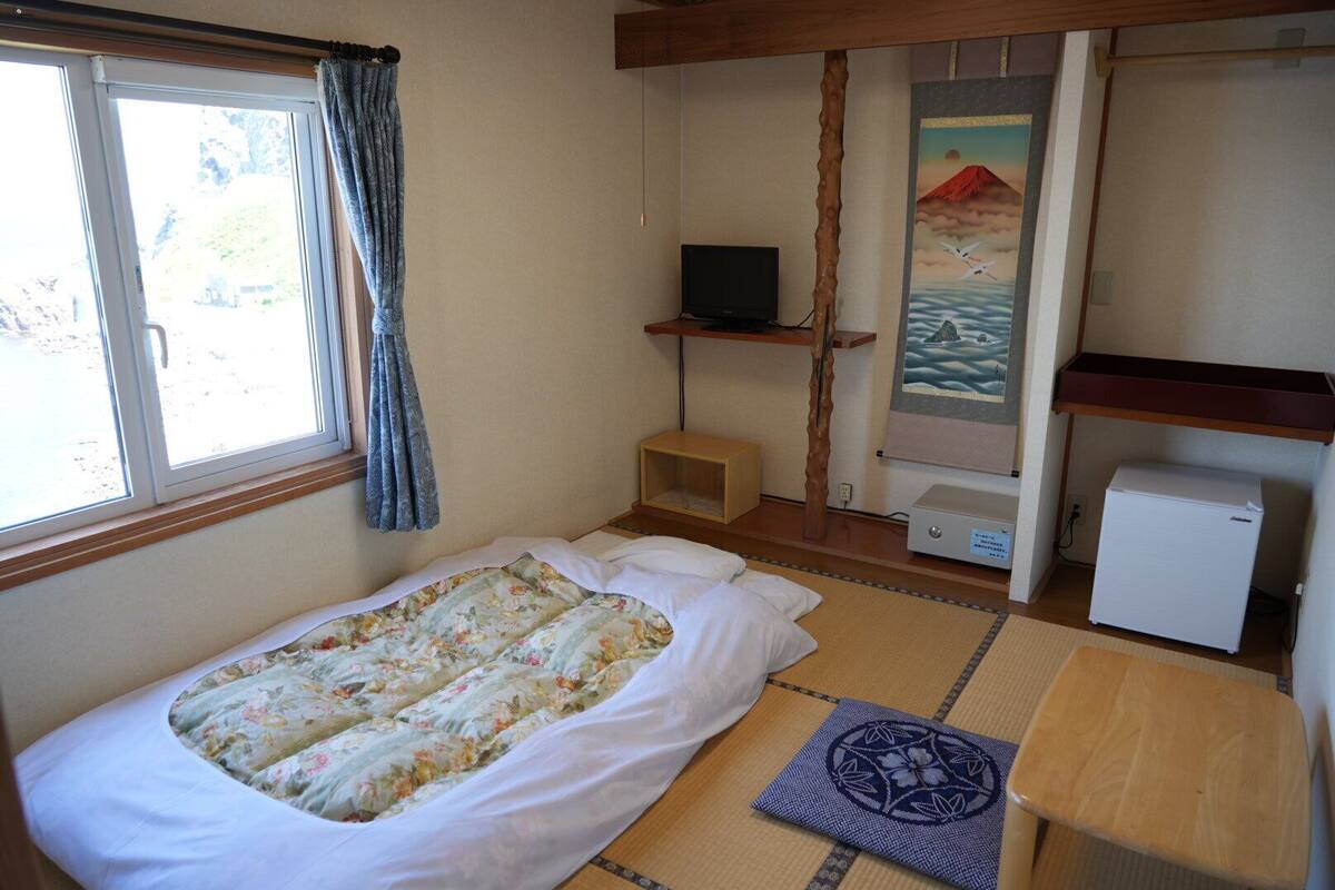 Una habitaci ón con cama, televisor, refrigerador pequeño y un cuadro de un paisaje montañoso.