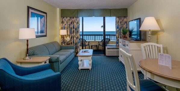Ett hotellrum med en soffa, ett litet bord, en tv och utsikt över havet.