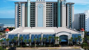 A large hotel with multiple floors, a prominent clock tower, and a view of the ocean.