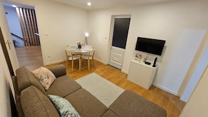 A living room with a sofa, a dining table with chairs, a TV, and a cabinet.