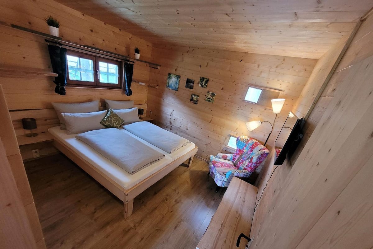 Ein Schlafzimmer in einer Holzhütte mit Bett, Stuhl und kleinem Tisch.