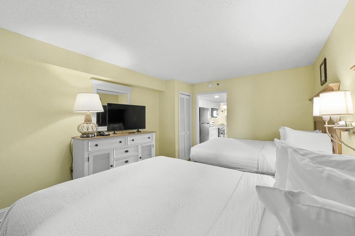Une chambre d’hôtel avec deux lits, une télévision, une commode et une lampe.