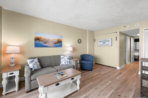 Una habitación con sofá, sillón, mesa de centro, lámpara, cuadro y un cartel que indica que es una casa de playa.