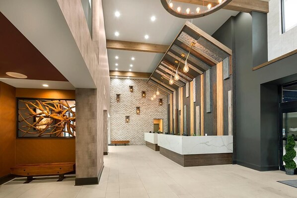 A modern lobby with a reception desk, a bench, a wall with a natural wood sculpture, and a brick wall with recessed lighting.