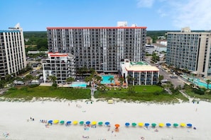 A hotel complex with multiple high-rise buildings, a swimming pool, and a beach area with umbrellas.