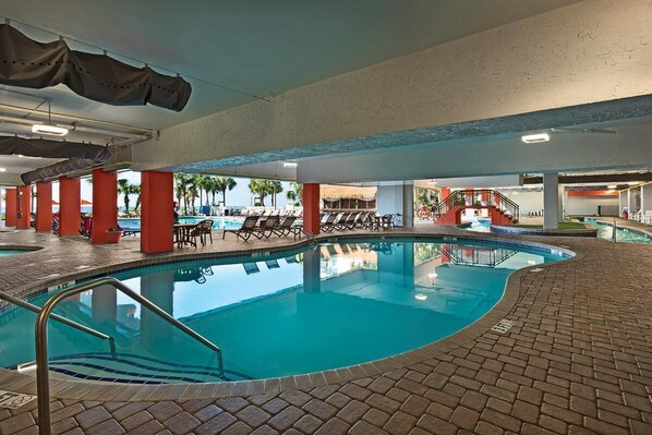 Una piscina interior con suelo de baldosas, pilares rojos y sillones de descanso.