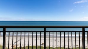 Une vue sur la plage depuis un balcon doté d’une balustrade, avec une plage de sable et l’océan en toile de fond.