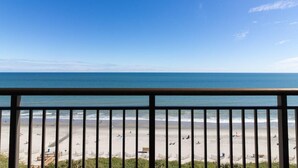 A beach view from a balcony with a railing, sandy beach, and ocean.