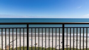 A beach view from a balcony with a railing, sandy beach, and ocean.