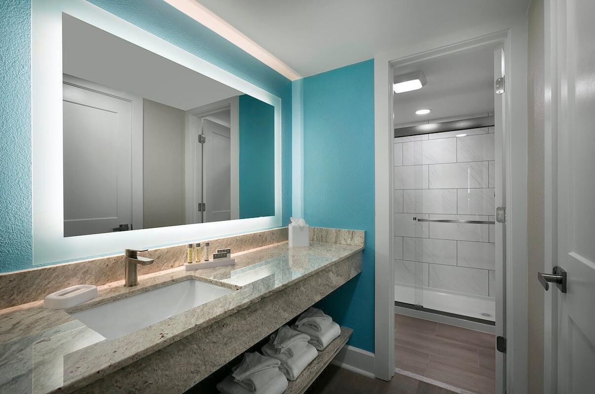 Un baño moderno con un espejo grande, dos lavamanos y una zona de ducha.