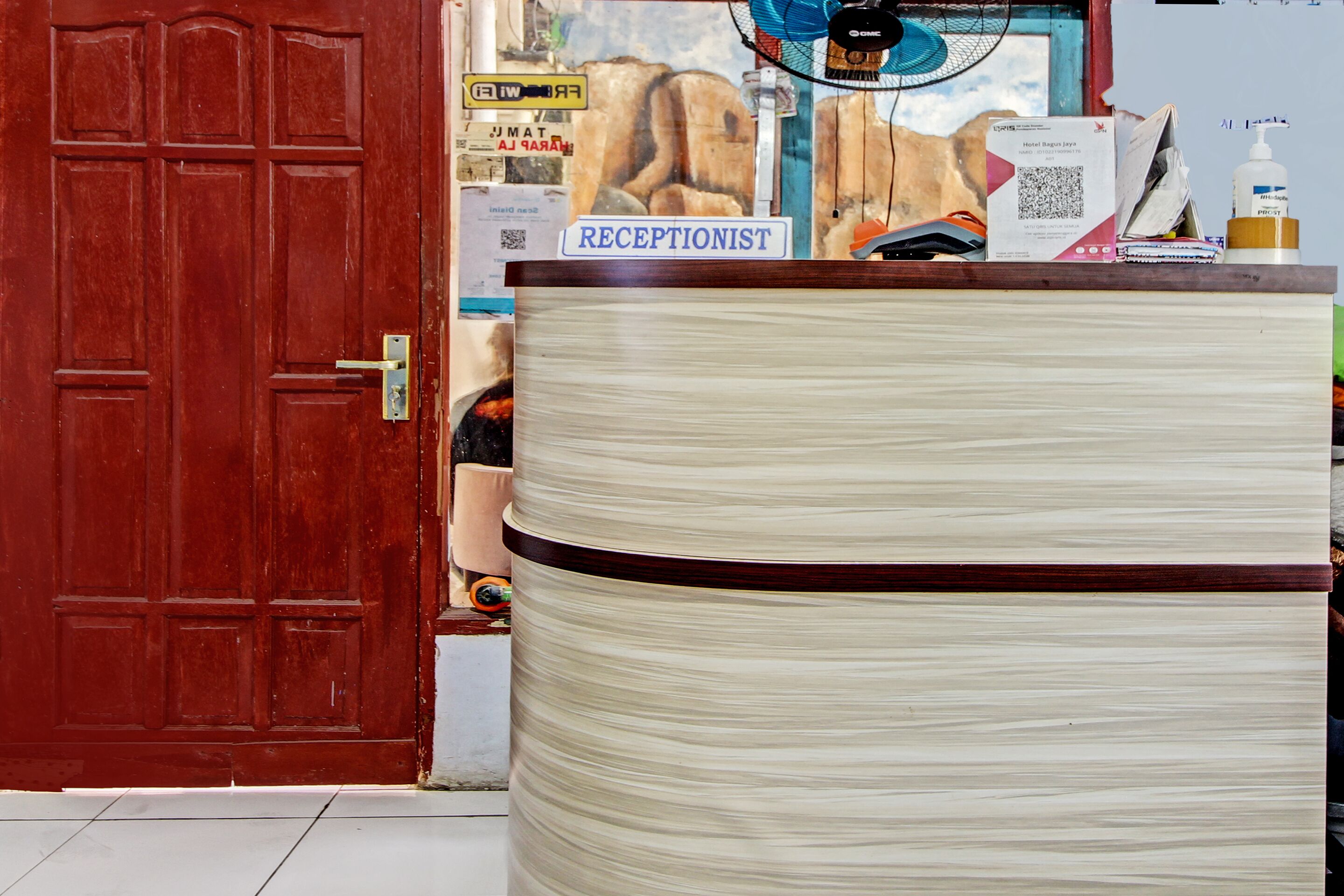 A reception desk with a sign reading "RECEPTIONIST," a fan, a water dispenser, and various papers and notices on the counter.