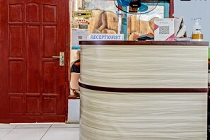 A reception desk with a sign reading "RECEPTIONIST," a fan, a water dispenser, and various papers and notices on the counter. - Hotel O Bagus Jaya Hotel (Ambarawa)