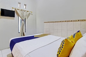 A neatly made bed with a blue and white bedspread, a patterned curtain, and a tiled wall with a decorative border. - Hotel O Bagus Jaya Hotel (Ambarawa)