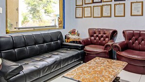 A room with a black leather sofa, a red leather armchair, and a patterned ottoman. There are framed certificates on the wall and a window with a view of trees. - Hotel O Bagus Jaya Hotel (Ambarawa)