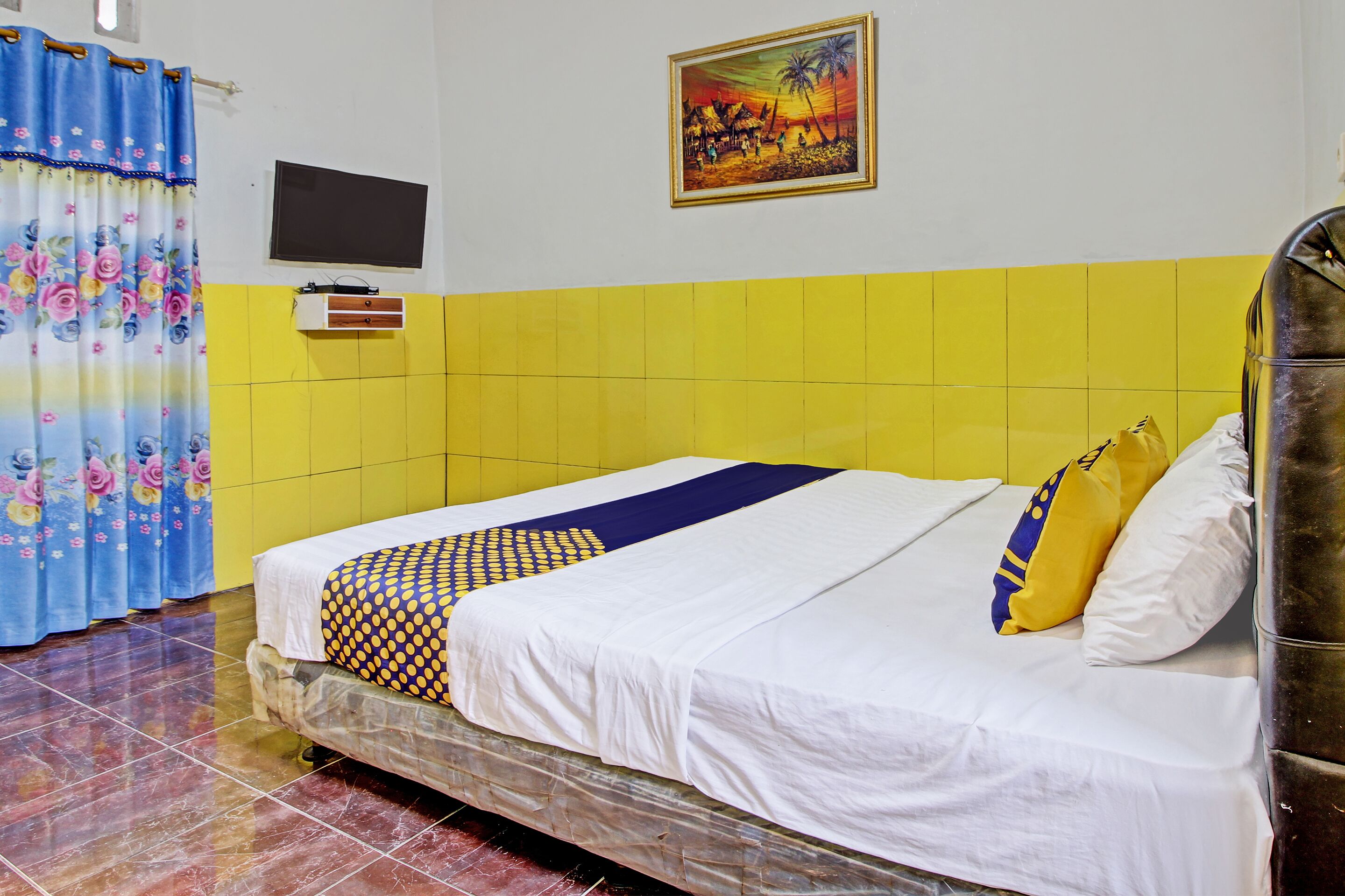 Habitación de hotel con cama, televisor, un cuadro y baño con azulejos amarillos.