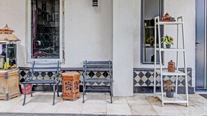 A tiled patio with two black metal benches, a wooden cabinet, and a white metal shelf with potted plants. - Hotel O Bagus Jaya Hotel (Ambarawa)