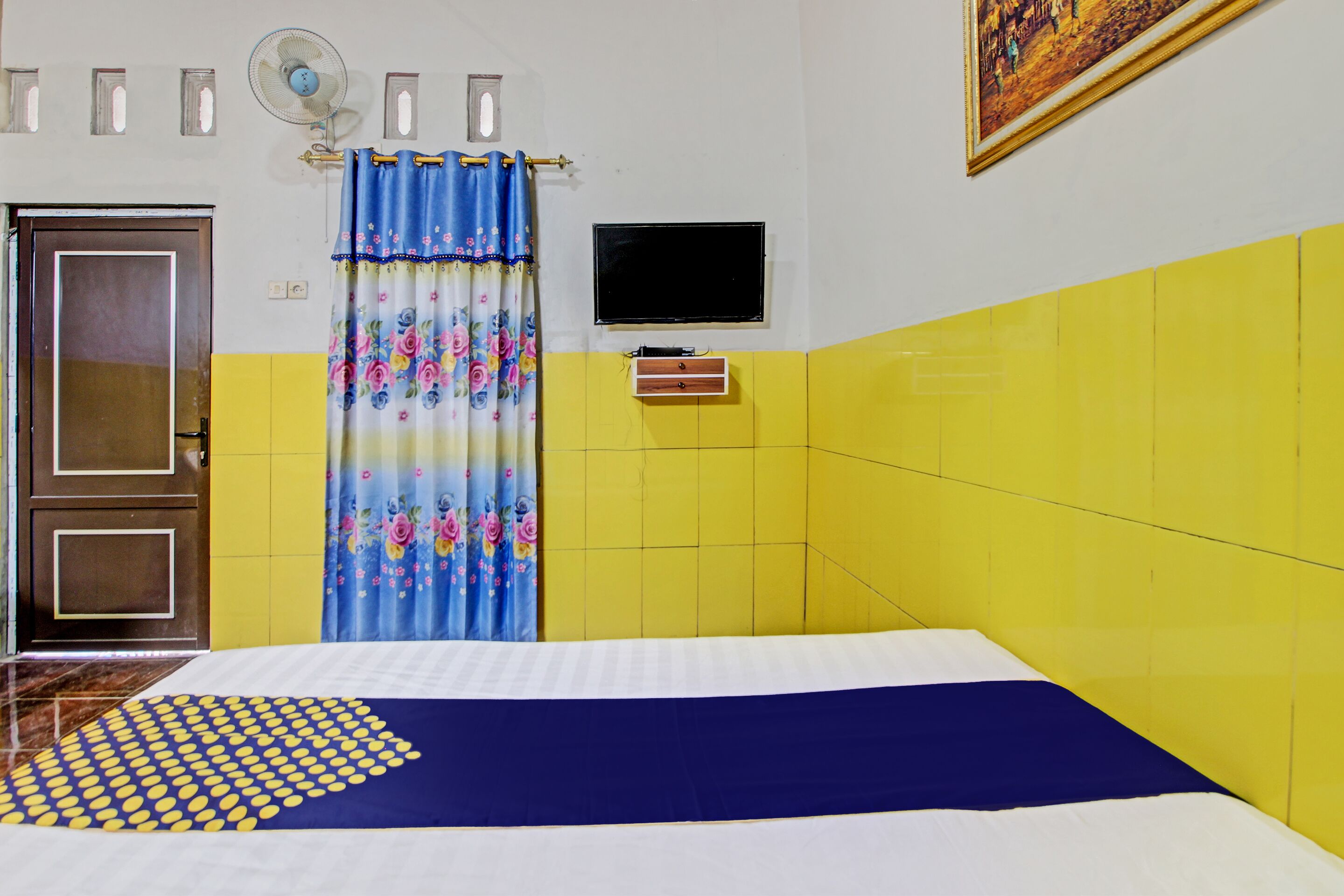 Una habitación con una cama, un televisor montado en la pared, una puerta y una cortina.