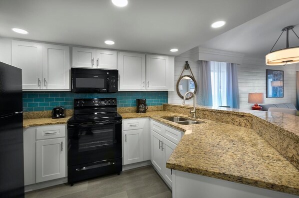 A modern kitchen with white cabinets, a black stove, a microwave, and a granite countertop.