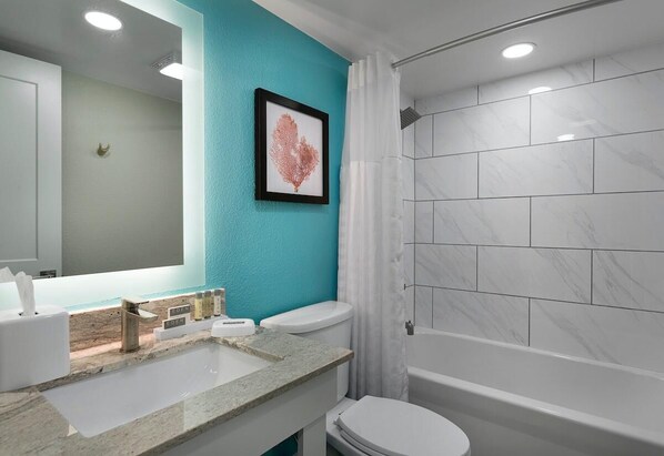 A bathroom with a turquoise wall, a white sink with a marble countertop, a framed artwork, a toilet, and a shower with white tiles.