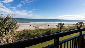 A beach view from a balcony with a railing, palm trees, and a clear sky. - Oceanfront Efficiency Beach Access Low Flr (Myrtle Beach)