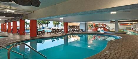 An indoor swimming pool with tiled flooring, red pillars, and lounge chairs.