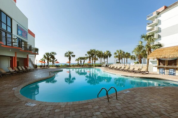 A swimming pool with lounge chairs and palm trees, surrounded by buildings with balconies.