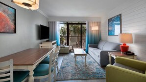 A modern hotel room with a dining area, a sofa, a TV, and a balcony with a view of palm trees. - Partial OV Suite - Your Coastal Getaway 4th Floor (Myrtle Beach)