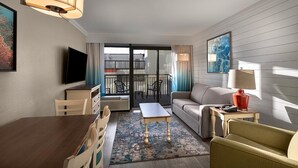 Een hotelkamer met een zithoek, een bank, een televisie en een balkon met uitzicht op de stad.