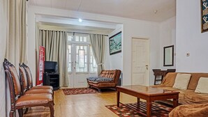 A living room with a wooden floor, a brown leather sofa, a brown leather chair, a wooden coffee table, and a television on a stand. - SPOT ON 91225 Kota Bunga Homestay Syariah (Cipanas)