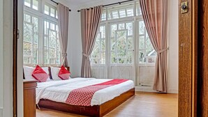 A spacious bedroom with a large bed, wooden headboard, and a view of the outdoors through large windows. - SPOT ON 91225 Kota Bunga Homestay Syariah (Cipanas)