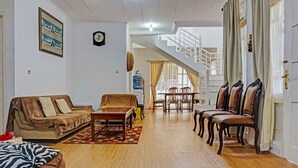 A spacious living room with a sofa, a coffee table, and a dining area with chairs. A staircase is visible in the background leading to an upper floor. - SPOT ON 91225 Kota Bunga Homestay Syariah (Cipanas)