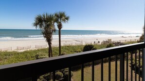 A beach view from a balcony with palm trees and a wooden deck.