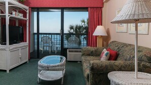 Ein Zimmer mit Balkon, ein Korbstuhl, eine Couch, ein Fernseher und eine Lampe.