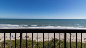 Blick auf einen Strand mit klarem Himmel, Sand und einem Zaun im Vordergrund.