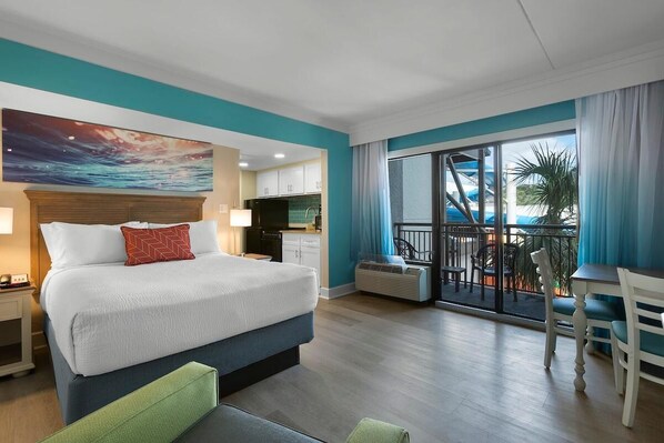 A hotel room with a bed, a desk, a balcony with a view, and a kitchen area.