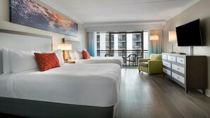 Habitación de hotel con dos camas, televisor, escritorio, silla y balcón con vistas.