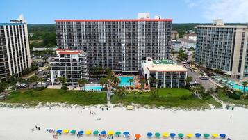 A hotel with multiple high-rise buildings, a central pool area, and a beach with umbrellas.